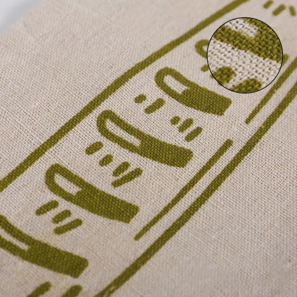 Close-up of the Levainry bread bag cloth: a fine, even natural-fibre weave the colour of raw oatmeal, with the olive loaf motif printed flat into it and an inset magnifying the threads